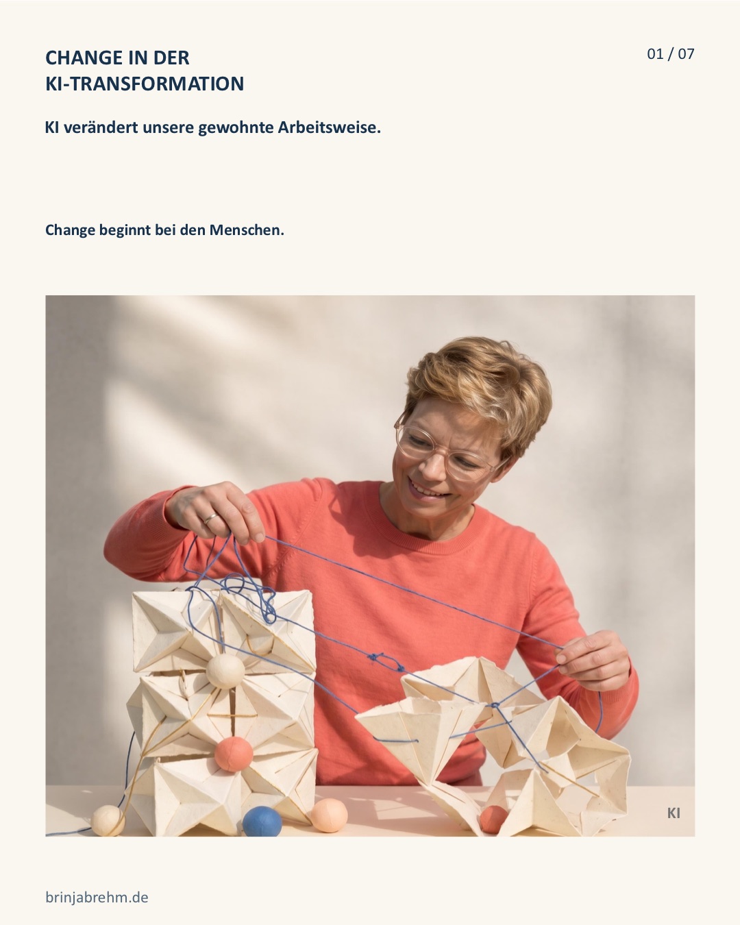 Brinja Brehm in einem korallenroten Pullover verbindet gefaltete Papierwürfel mit blauen Fäden. Erste Folie ihres LinkedIn-Karussells zur KI-Transformation.